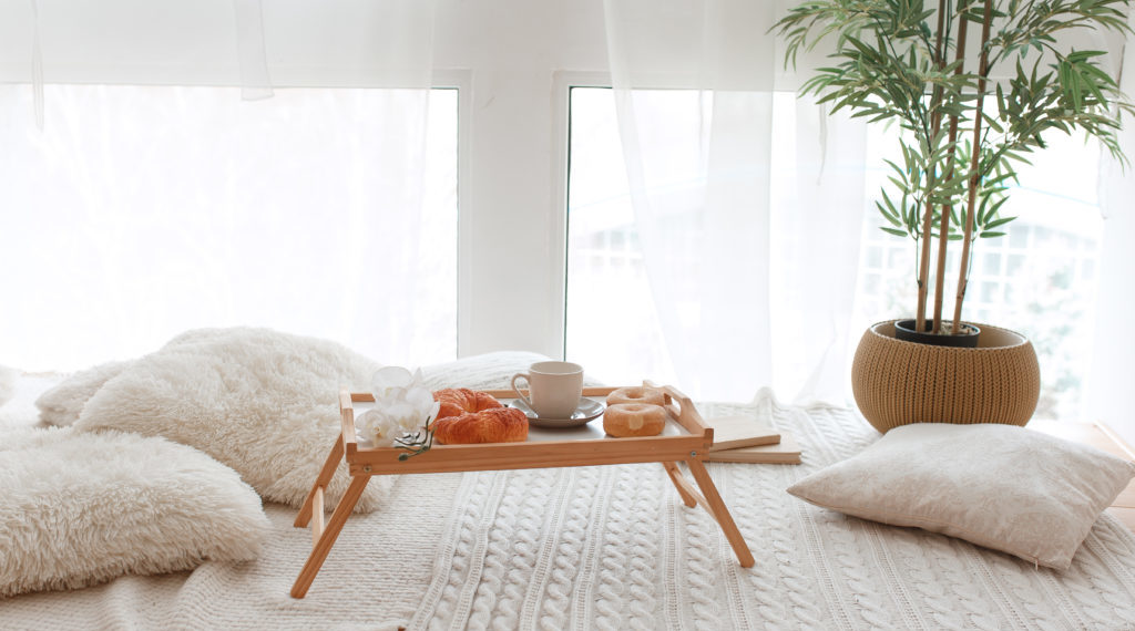 Breakfast on wooden tray. Blank cup, croissants, donuts standing in front of big window on knitted covering.