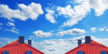 Red roof of new detached houses against blue sky.