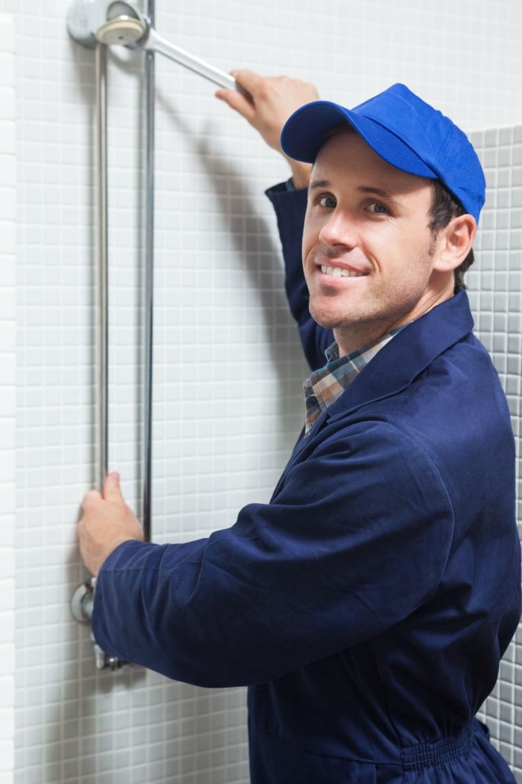 Smiling plumber repairing shower head in public bathroom