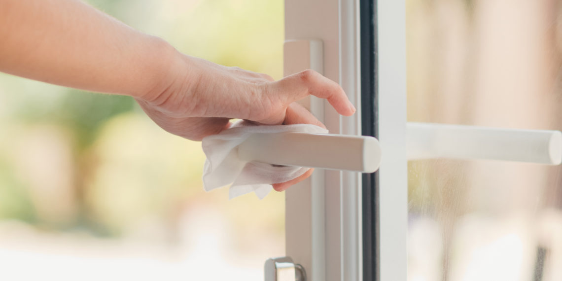 Asian woman using alcohol spray on tissue clean doorknob before open door for protect coronavirus. Female clean surface for hygiene when social distancing stay at home and self quarantine time.