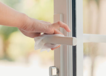 Asian woman using alcohol spray on tissue clean doorknob before open door for protect coronavirus. Female clean surface for hygiene when social distancing stay at home and self quarantine time.