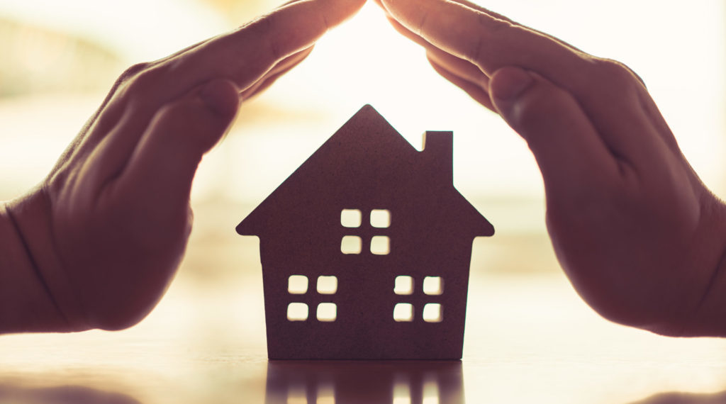 Hands of a young woman surround a wood house model. Real estate agent offer house, property insurance and security, affordable housing concepts