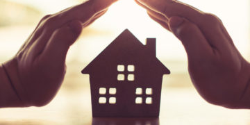 Hands of a young woman surround a wood house model. Real estate agent offer house, property insurance and security, affordable housing concepts