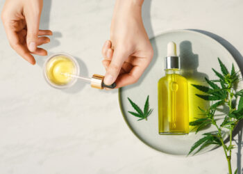 Pipette with CBD cosmetic oil in female hands on a table background with a bottle of cannabis oil and hemp leaves, marijuana