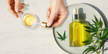 Pipette with CBD cosmetic oil in female hands on a table background with a bottle of cannabis oil and hemp leaves, marijuana