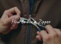 A close-up of hands repairing a stuck zipper on a jacket, with tools like pliers and wax nearby, realistic.