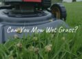 A lawnmower struggling to cut wet grass, clumps of grass sticking to the blades, damp green lawn, cloudy sky, realistic.